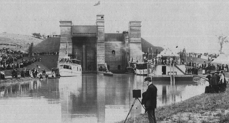 Historical photo, photographer on shoreline in foreground, hydraulic lift lock in background on a canal
