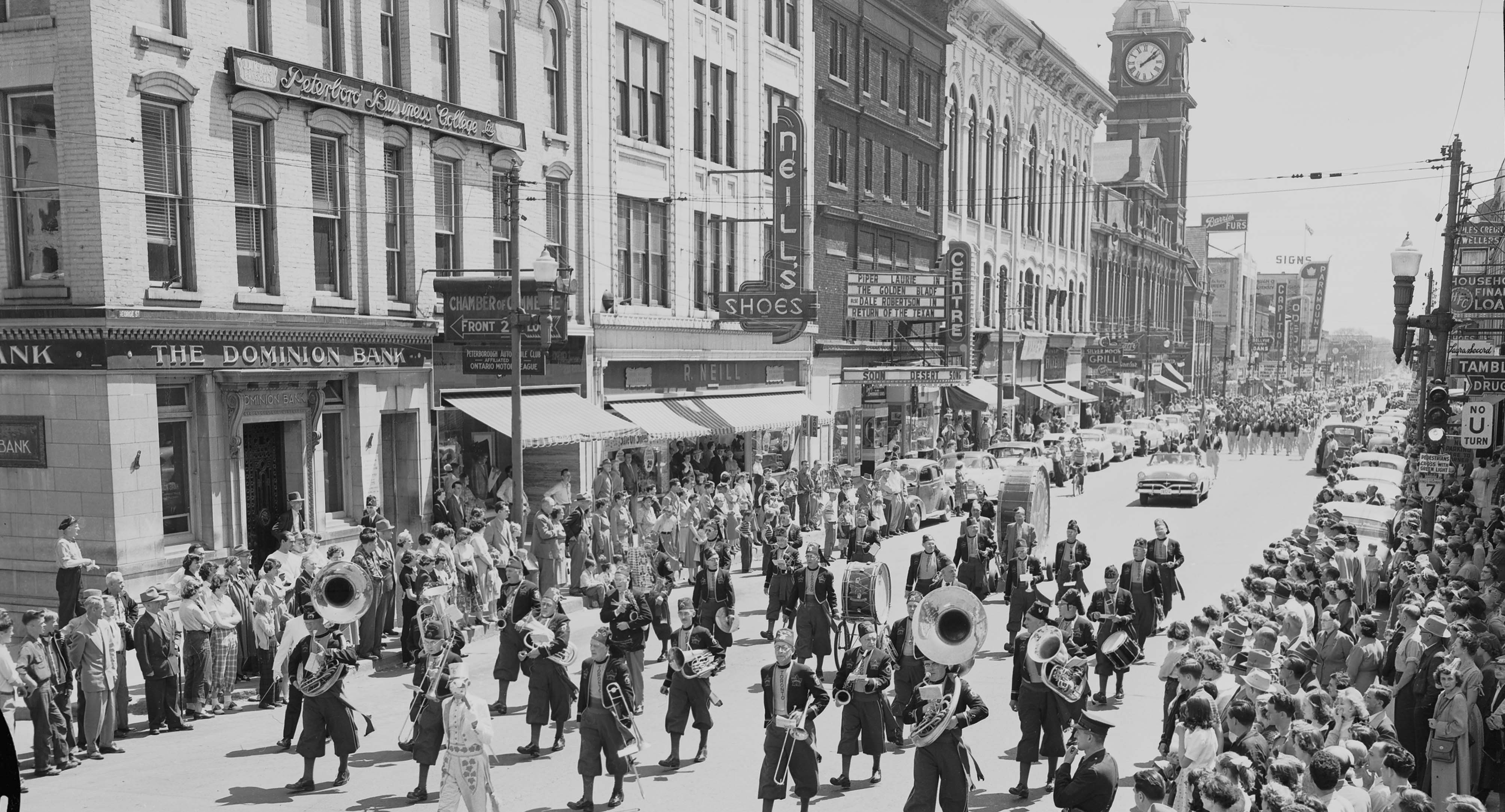 Historic photo, black and white image, band walking down a downtown street, crowds along the street