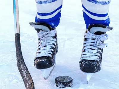 Close up of hockey skates on the ice with a stick and puck